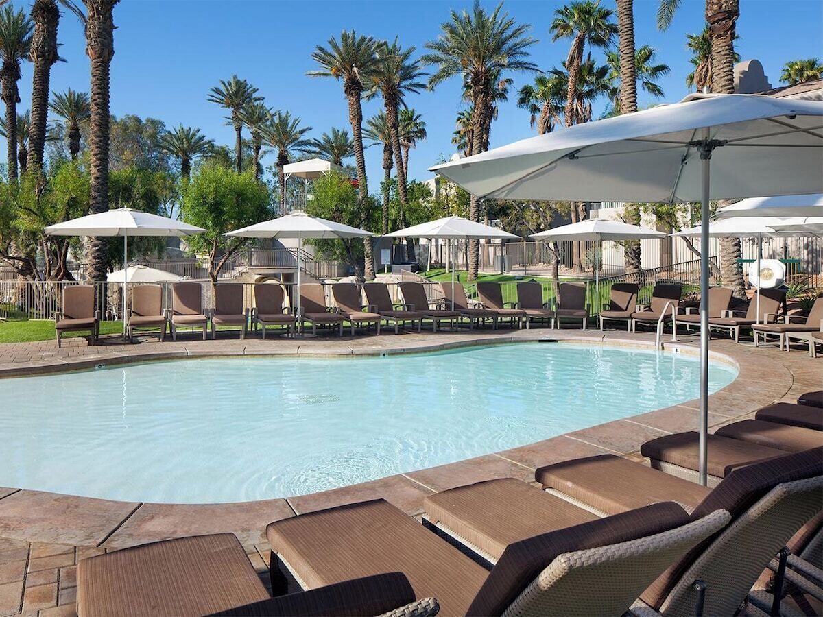 A pool area with lounge chairs and umbrellas, surrounded by palm trees.