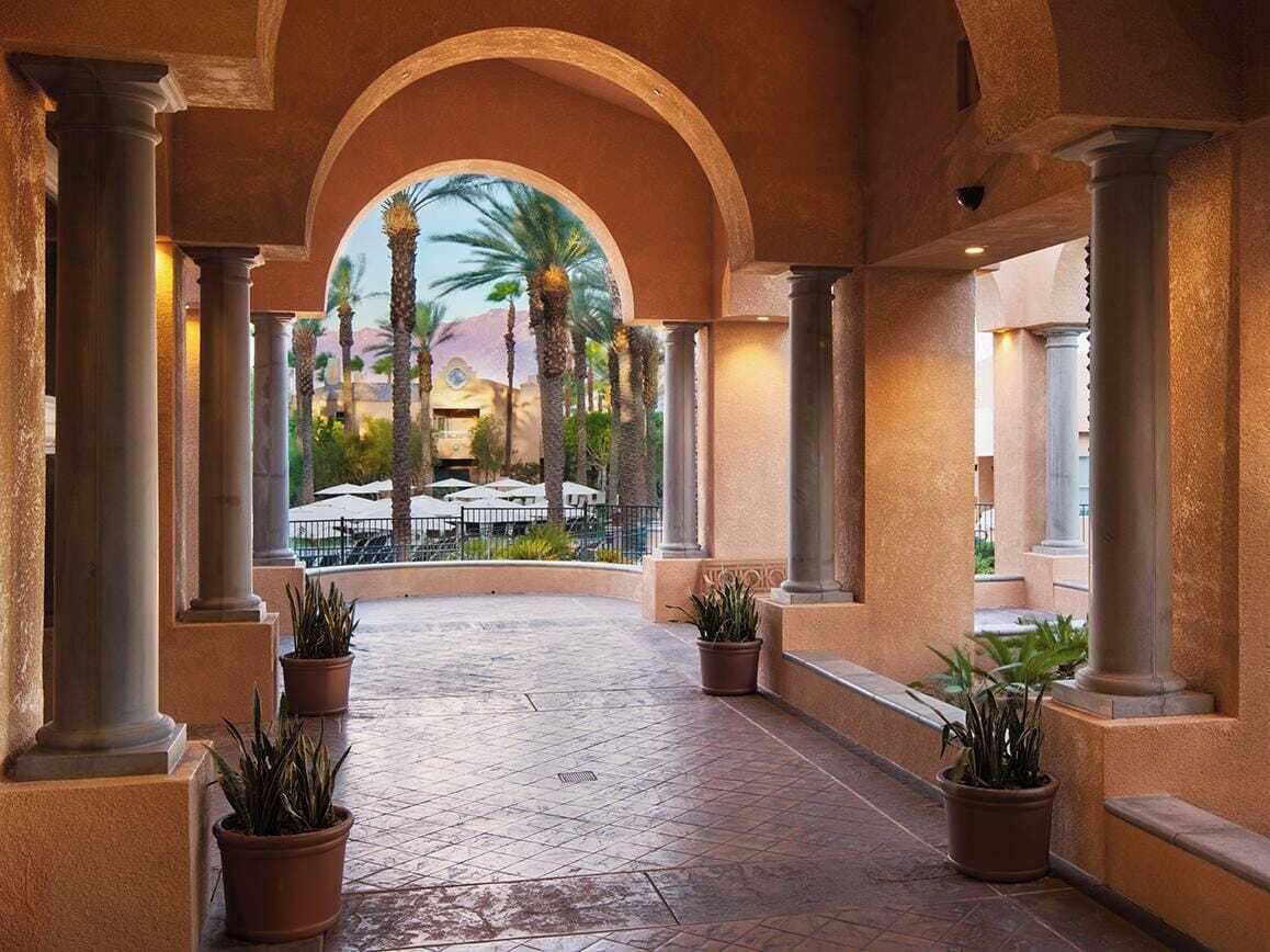 A covered outdoor area with columns, potted plants, and a view of a resort area.