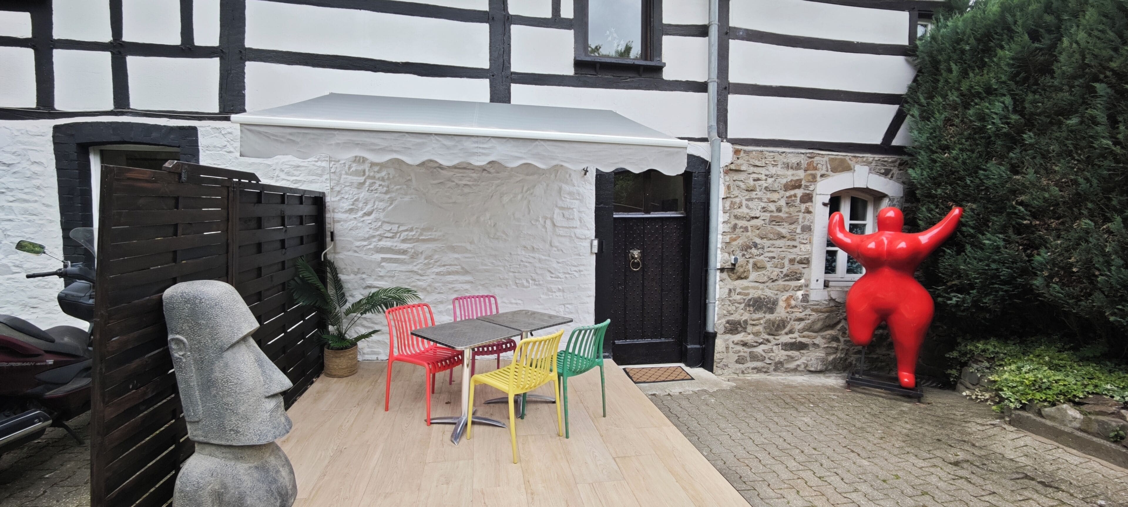 A courtyard with a table and chairs, a statue, and a red sculpture.