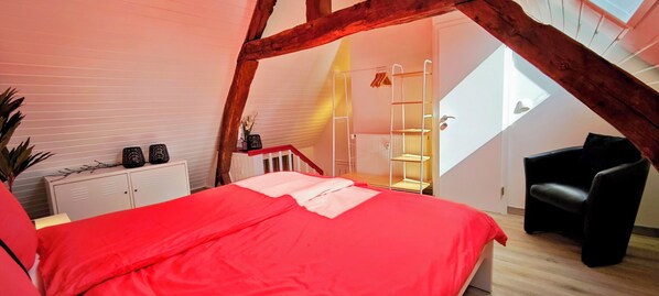 A bedroom with a red bedspread, a white dresser, a black chair, and a skylight.