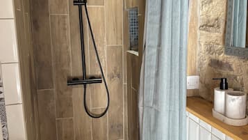 A shower with a handheld showerhead and a rain shower head, a towel rack, and a mirror with a decorative frame.