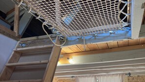 Una scala in legno conduce a una zona mansardata con soffitto a rete, una cucina con finestra e un muro in pietra.
