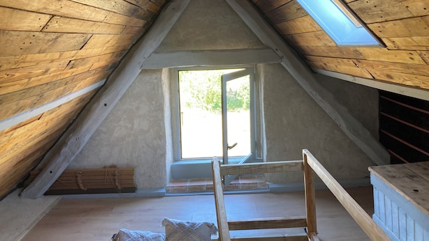 Una stanza mansardata con travi in legno, un velux e una finestra.