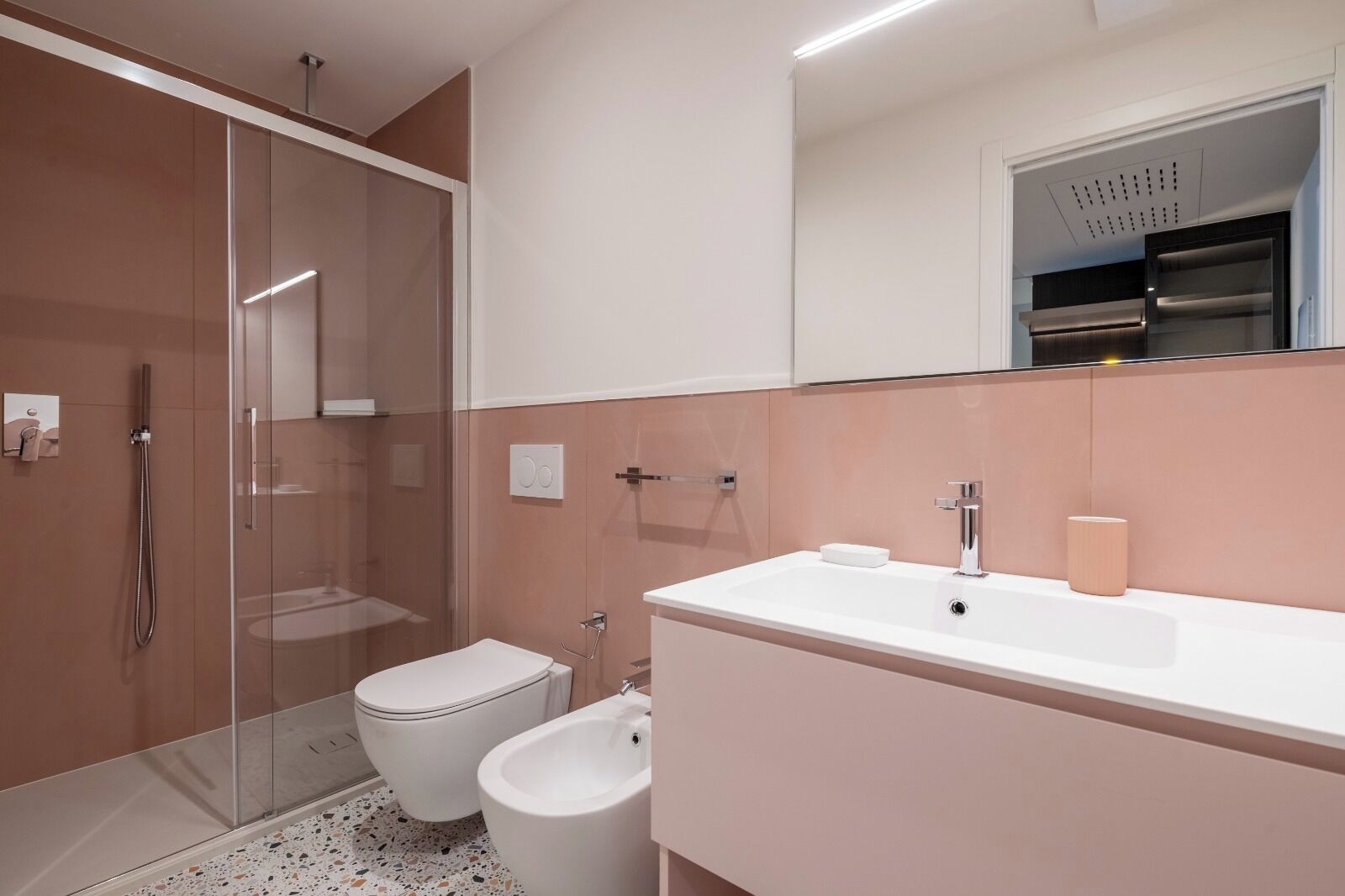 Un baño moderno con ducha de vidrio, inodoro, bidé y tocador con espejo.