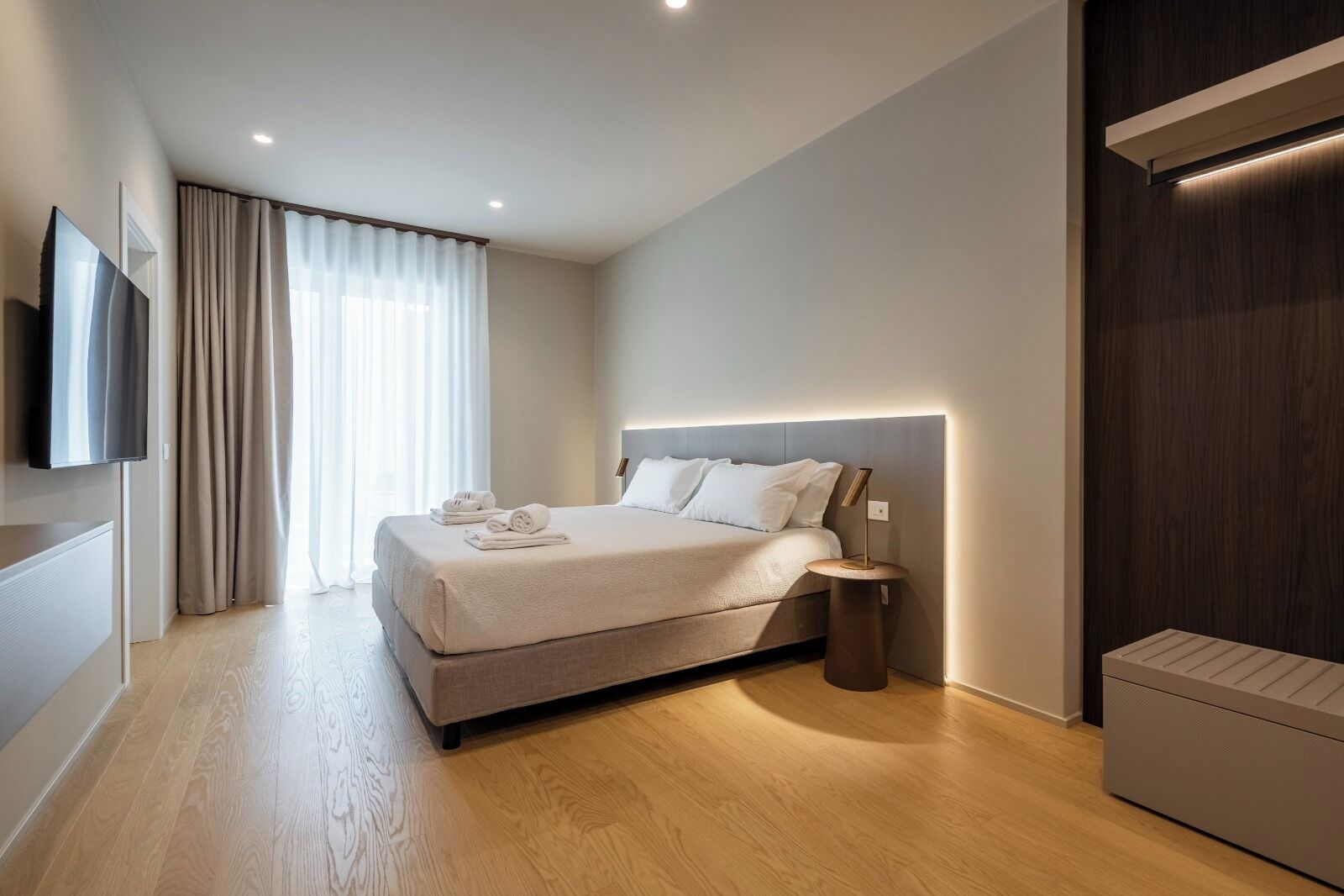 Um quarto moderno com uma cama grande, uma mesa de cabeceira, uma TV de tela plana e um armário embutido.