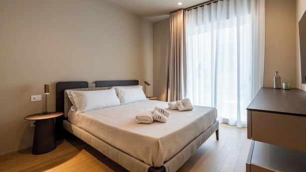 A hotel room with a bed, bedside lamp, curtains, and a desk with a bottle and a glass. - Ardito White Coast Collection (Polignano a Mare)