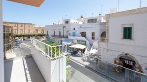 A balcony with a view of a street, a café, and a shop with bags. - Ardito White Coast Collection (Polignano a Mare)