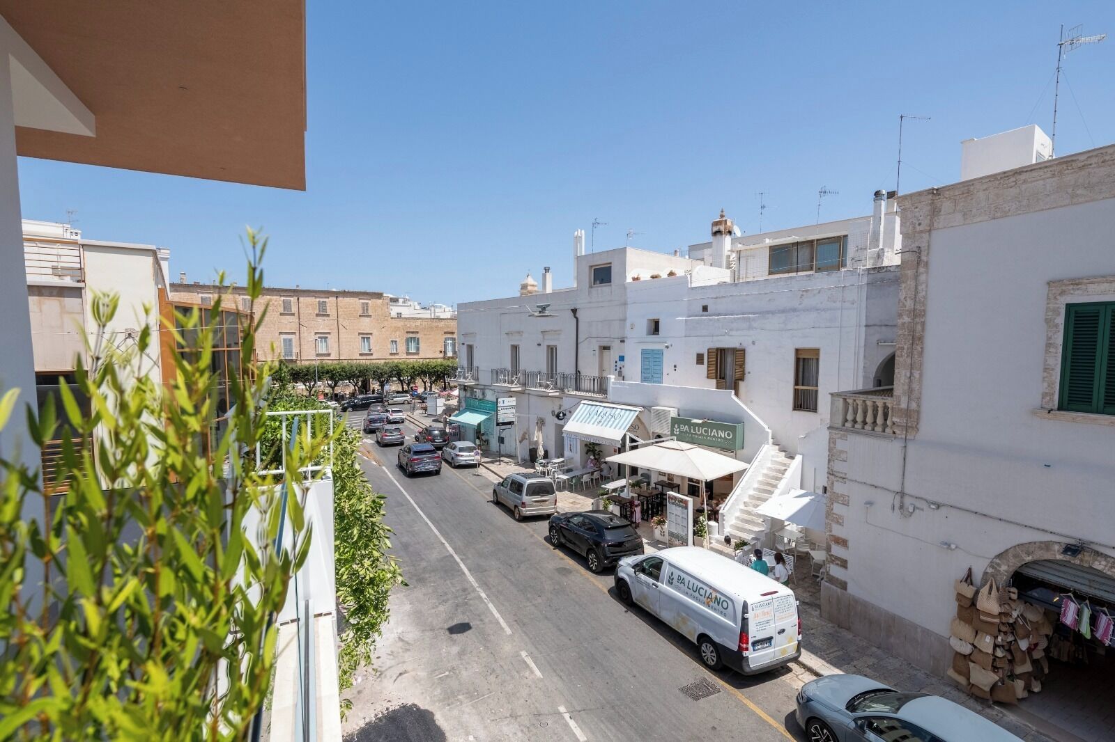 Une vue de rue avec des voitures garées, un fourgon blanc et des bâtiments avec des enseignes.