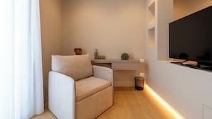 A modern living room with a sofa, a flat-screen TV, a small shelf with decorative items, and a waste bin. - Ardito White Coast Collection (Polignano a Mare)