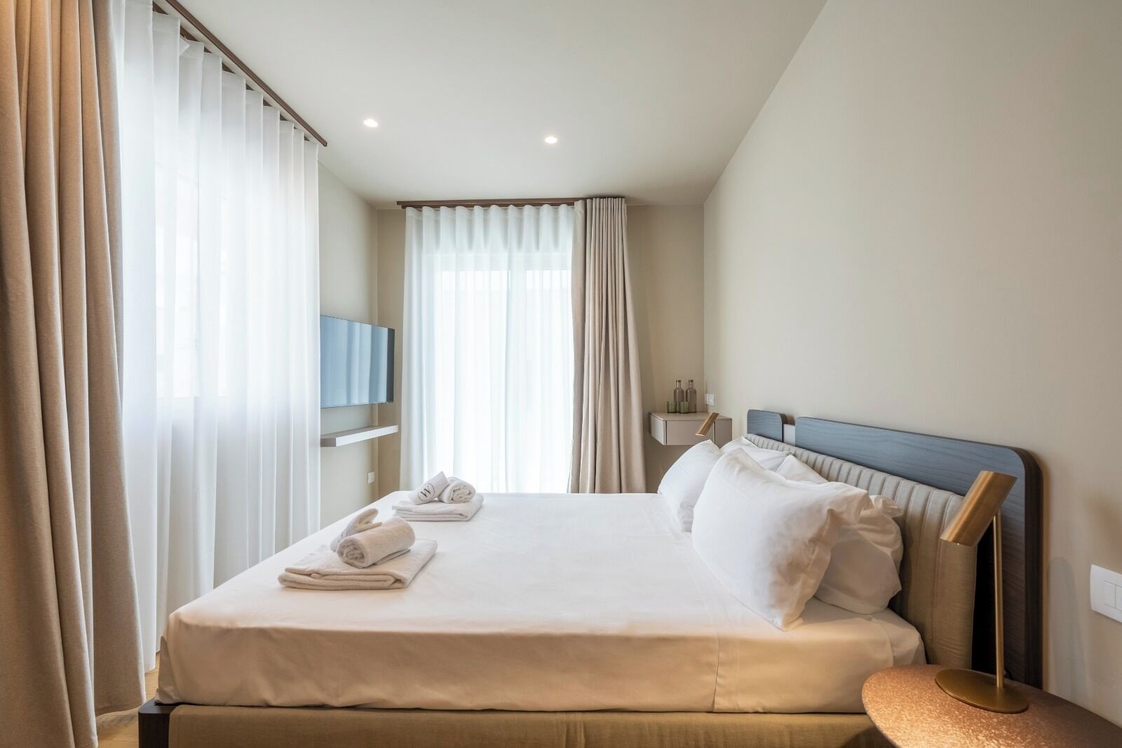 Ein Hotelzimmer mit einem Bett, einem Nachttisch, einer Lampe und einem Fernseher an der Wand.