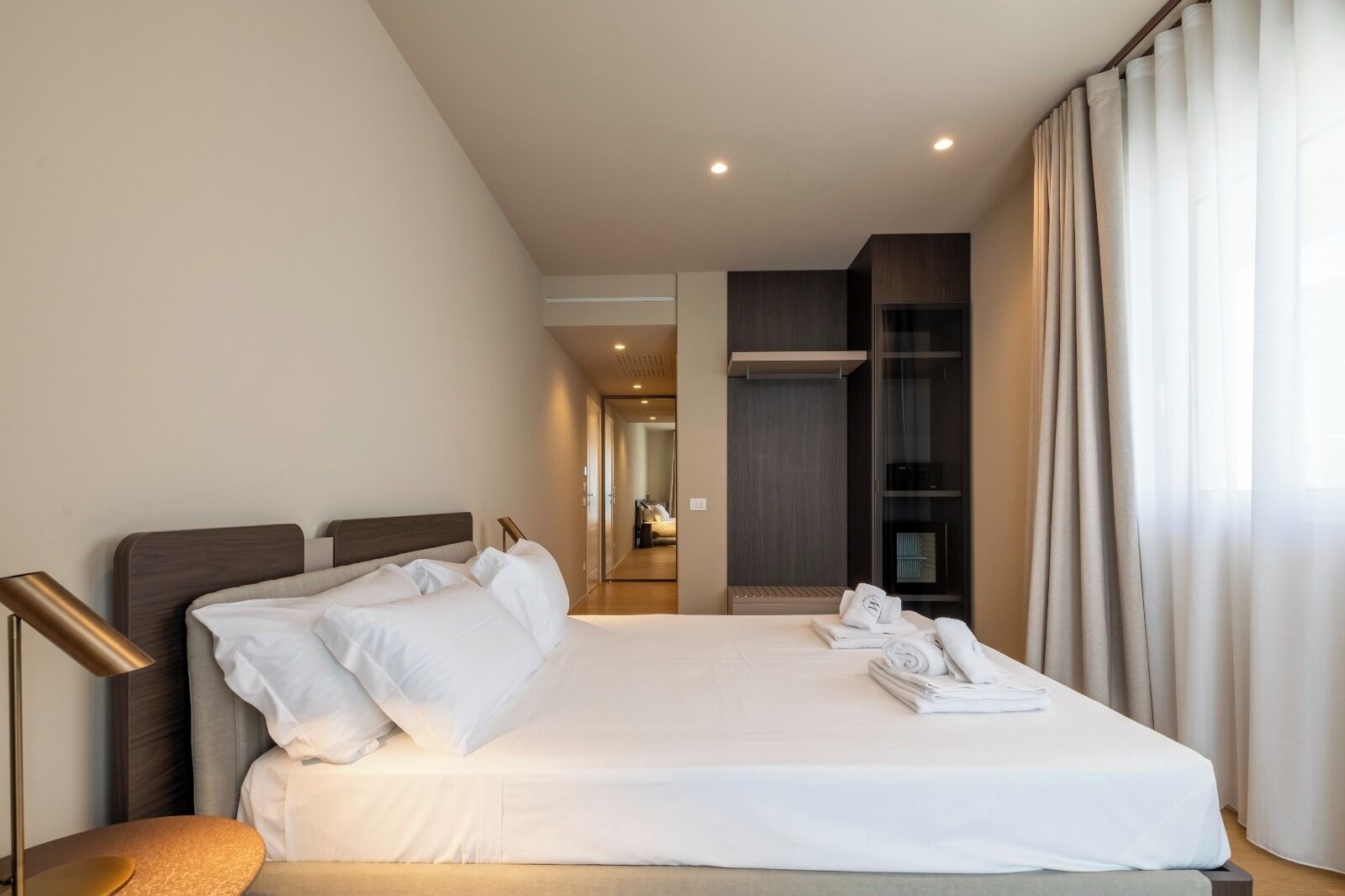Een hotelkamer met een groot bed, een bedlampje, een kledingkast en uitzicht op de gang.