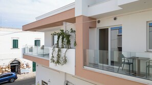 Un bâtiment moderne doté d’un balcon, d’une porte vitrée et d’un petit espace extérieur aménagé pour s’asseoir.