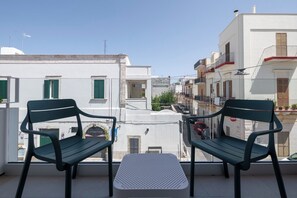A balcony with two green chairs and a small table, overlooking a street with buildings and parked cars. - Ardito White Coast Collection (Polignano a Mare)