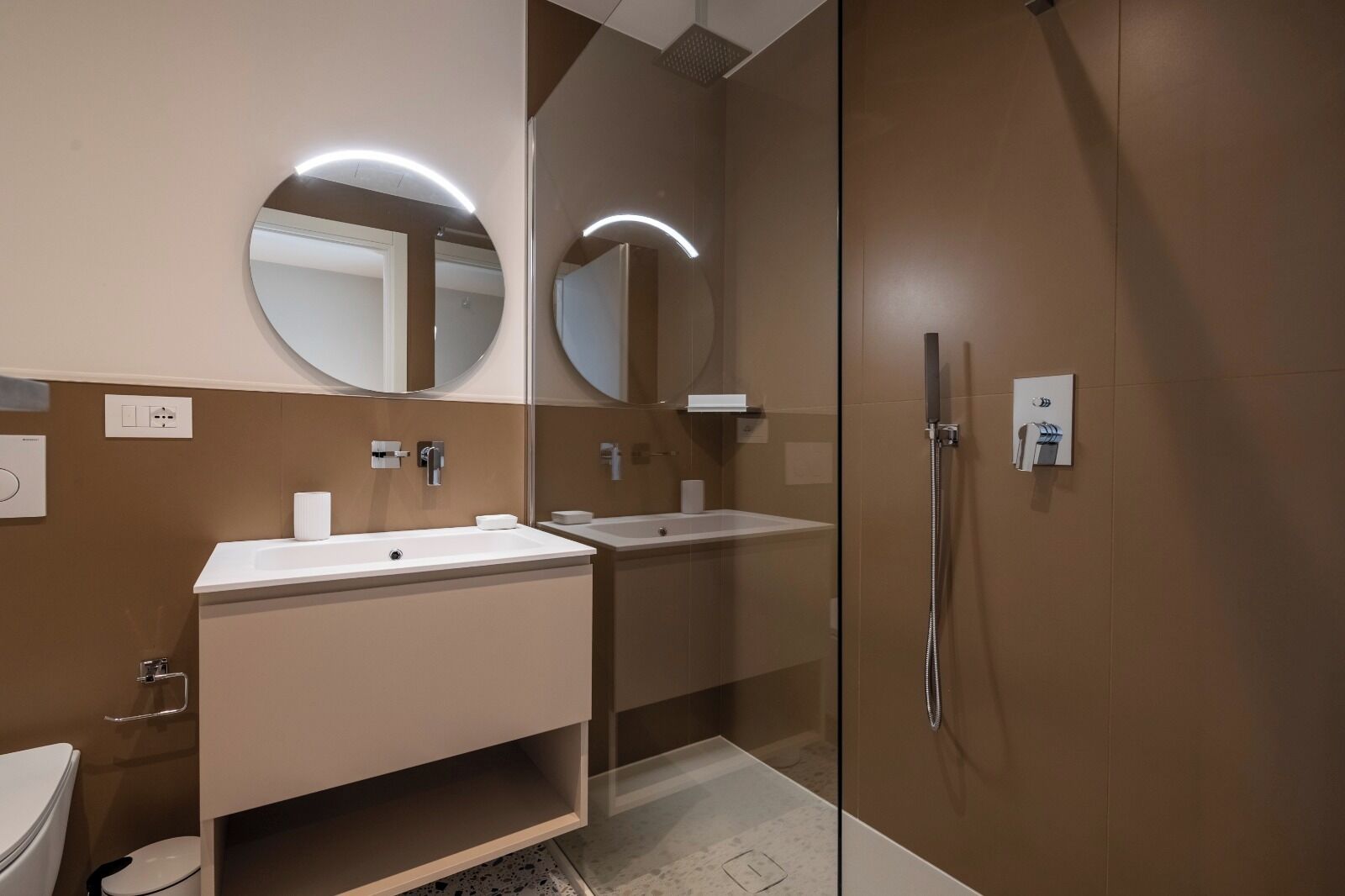 Un baño moderno con ducha envuelta en vidrio, dos lavamanos y un inodoro.