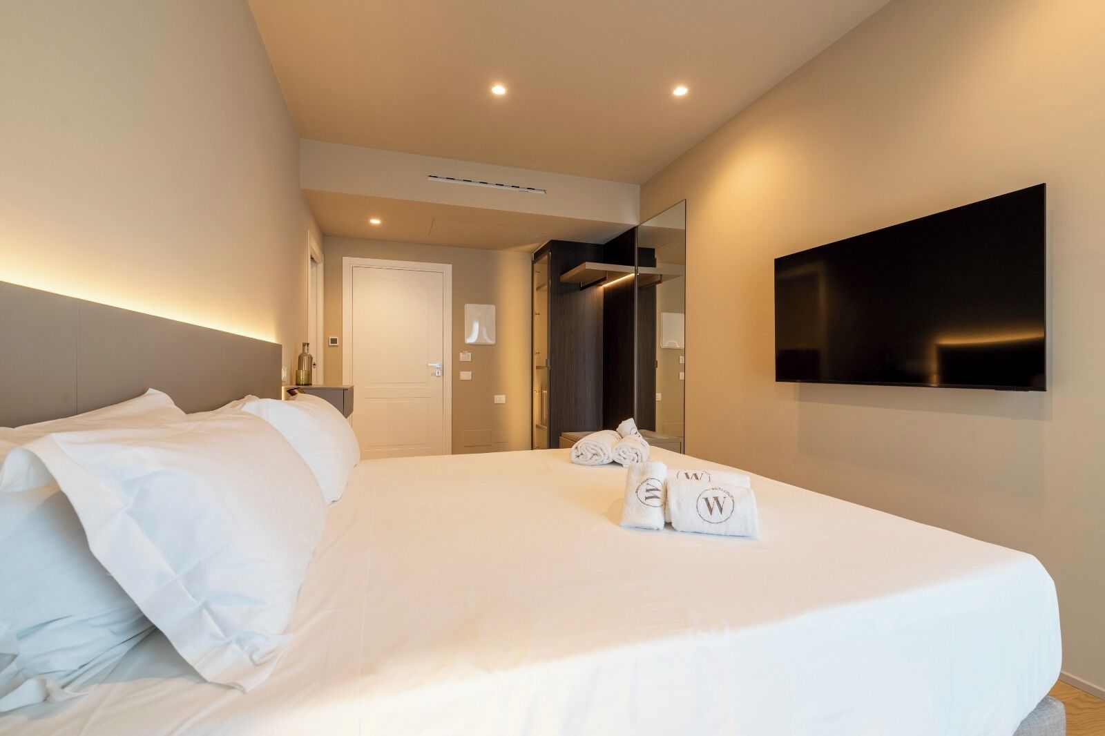 A hotel room with a large bed, a flat-screen TV mounted on the wall, and a door leading to a bathroom.