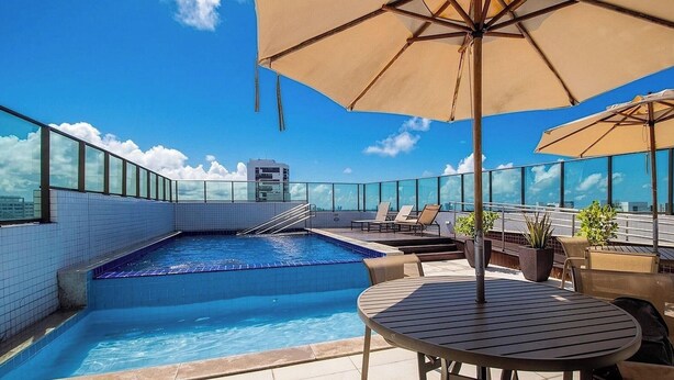 A rooftop pool area with a clear view of the city skyline, a swimming pool, lounge chairs, and umbrellas. - Studio in Condo. w/ Pool and City View Bcm0403 (Recife)