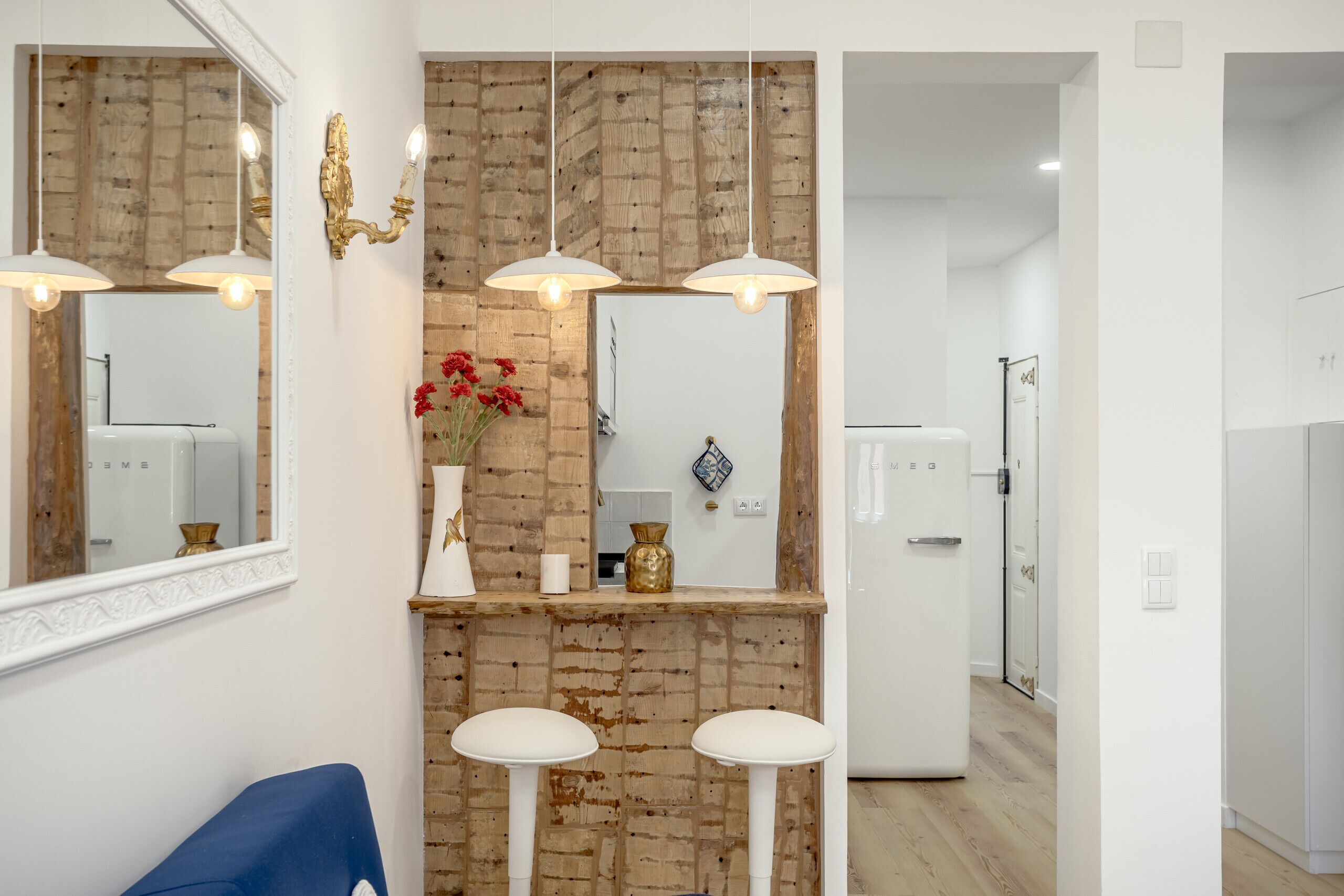 Un baño moderno con pared de ladrillo decorativa, un lavabo blanco y un espejo encima. Hay dos taburetes blancos y una silla azul.