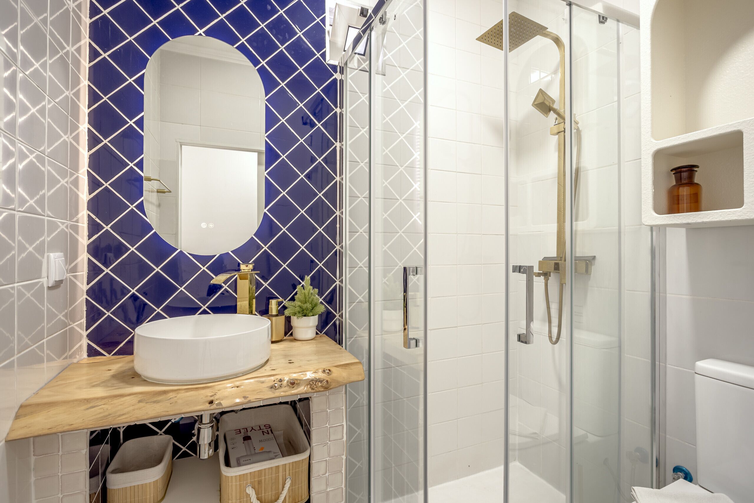 Un bagno con un lavandino bianco, uno specchio, una doccia con porta in vetro e una parete rivestita di piastrelle blu.