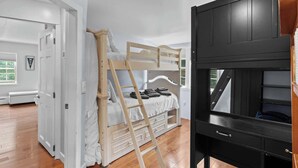 A room with a bunk bed, a wooden ladder, a black TV stand, and a white door.