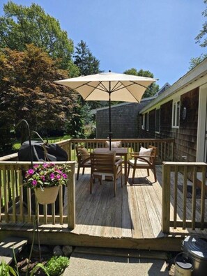 A wooden deck with a table and chairs, an umbrella, and a hanging flower pot. - Private 2BR Bungalow • Deck & Grill • Near Newport & RI Coastline  (North Kingstown)