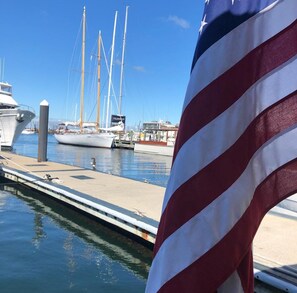 A marina with boats docked, a clear sky, and an American flag in the foreground. - Private 2BR Bungalow • Deck & Grill • Near Newport & RI Coastline  (North Kingstown)