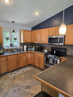 A kitchen with wooden cabinets, a microwave, a stove, and a sink. - Private 2BR Bungalow • Deck & Grill • Near Newport & RI Coastline  (North Kingstown)