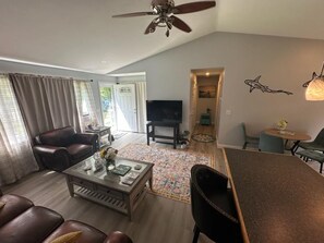A living room with a ceiling fan, leather sofas, a coffee table, and a TV. - Private 2BR Bungalow • Deck & Grill • Near Newport & RI Coastline  (North Kingstown)
