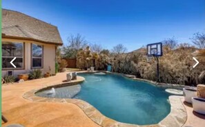 A swimming pool with a curved design, a basketball hoop, and a house with a thatched roof. - Luxury Pool Oasis  2 primary suites/5 rooms/10 beds. Perfect for multi families (San Antonio)