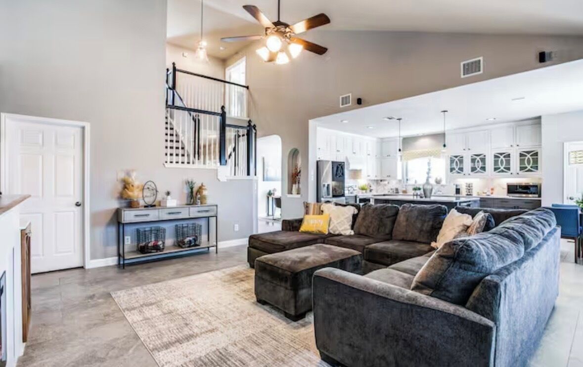 A spacious living area with a large sectional sofa, a ceiling fan, and a kitchen in the background.