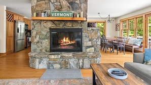 Ein Kamin aus Stein, ein Schild mit der Aufschrift Vermont, ein Essbereich mit Aussicht und eine Küche mit modernen Geräten.