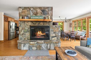 Ein Kamin aus Stein, ein Schild mit der Aufschrift Vermont, ein Essbereich mit Aussicht und eine Küche mit modernen Geräten.