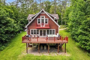 A two-story house with a deck, surrounded by dense greenery. - Luxury Okemo Lodge | 0.5 Mi to Slopes | Sleeps 14 (Ludlow)