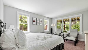 Ein Schlafzimmer mit einem großen Bett, zwei Nachttischen, einem Sessel, einem Schreibtisch und einem Fenster mit Blick ins Grüne.
