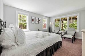 Ein Schlafzimmer mit einem großen Bett, zwei Nachttischen, einem Sessel, einem Schreibtisch und einem Fenster mit Blick ins Grüne.