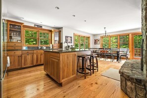 A spacious kitchen with wooden cabinets, a central island, and a dining area with a view of the outdoors. - Luxury Okemo Lodge | 0.5 Mi to Slopes | Sleeps 14 (Ludlow)