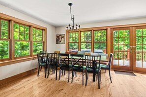 A dining area with a wooden table and chairs, large windows, and a view of greenery. - Luxury Okemo Lodge | 0.5 Mi to Slopes | Sleeps 14 (Ludlow)