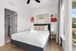 Ein Schlafzimmer mit einem Bett, einem Nachttisch mit Lampe, einem Fenster mit Vorhängen und einem Bild an der Wand.