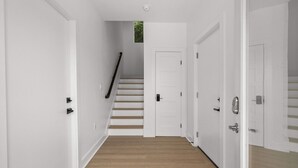 Un pasillo con paredes blancas, piso de madera y una escalera que lleva a una puerta.