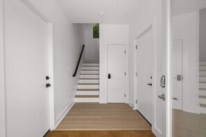 Ein Flur mit weißen Wänden, Holzboden und einer Treppe zu einer Tür.