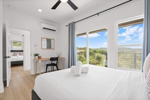A hotel room with a bed, a desk, a chair, a mirror, and a view of the outdoors. - Hilltop Home + Guest Casita w Sweeping Lake Travis Views from Your Rooftop Deck (Austin)