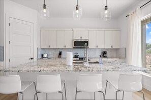 A modern kitchen with white cabinets, a granite countertop, and three pendant lights. - Hilltop Home + Guest Casita w Sweeping Lake Travis Views from Your Rooftop Deck (Austin)