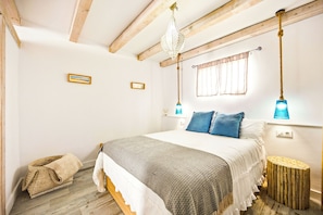 A bedroom with a wooden ceiling, a bed with white and blue bedding, a hanging light fixture, and a small window with curtains. - Charming Apartment in Vejer de la Frontera (Vejer de la Frontera)