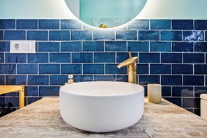 A bathroom with a white sink, a gold faucet, and blue-tiled walls. - Charming Apartment in Vejer de la Frontera (Vejer de la Frontera)