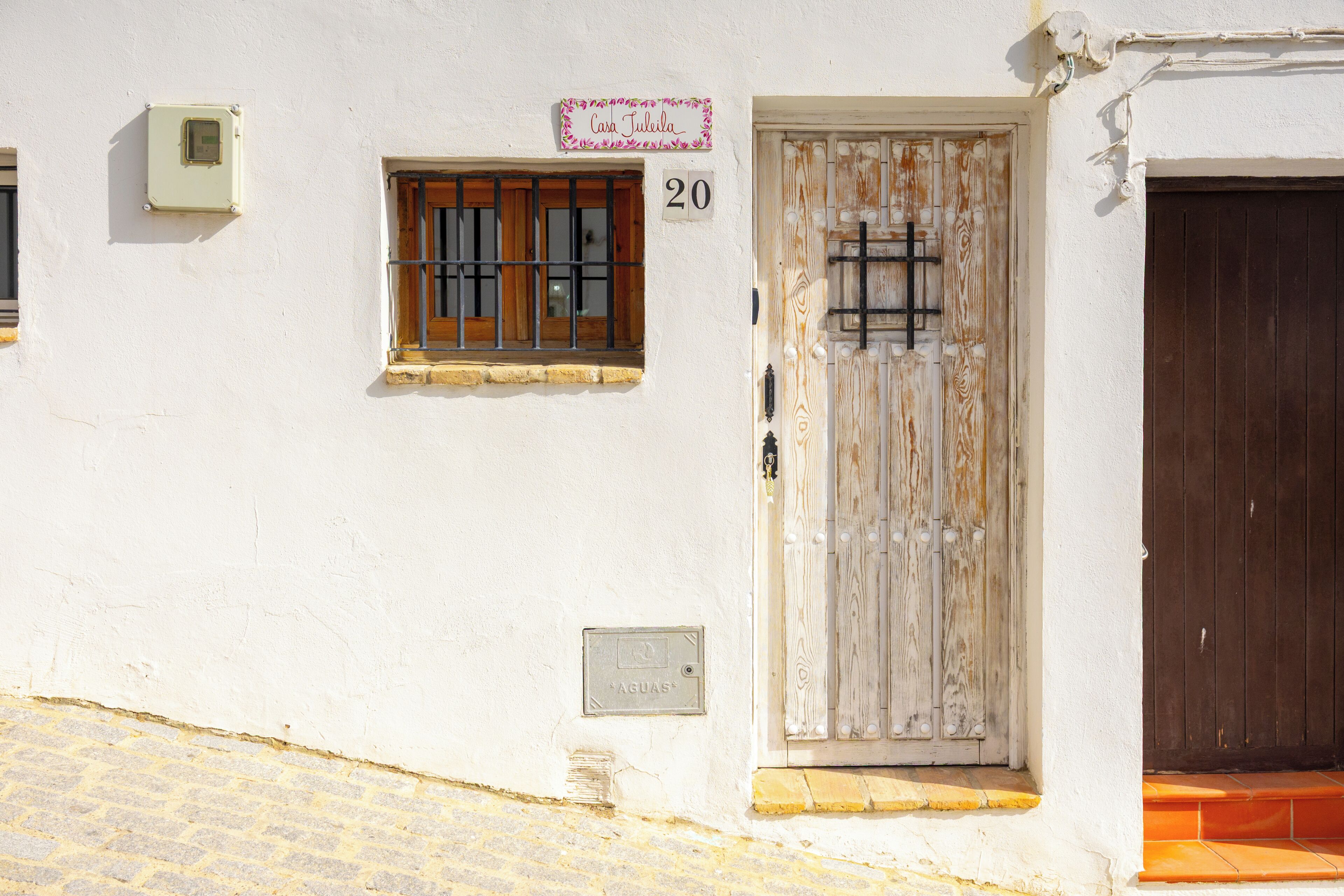Un edificio blanco con puerta de madera, una ventana con barrotes y un cartel sobre la puerta.