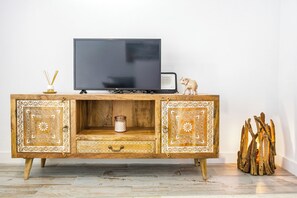 A wooden TV stand with a flat-screen TV, a small speaker, and decorative items. - Charming Apartment in Vejer de la Frontera (Vejer de la Frontera)