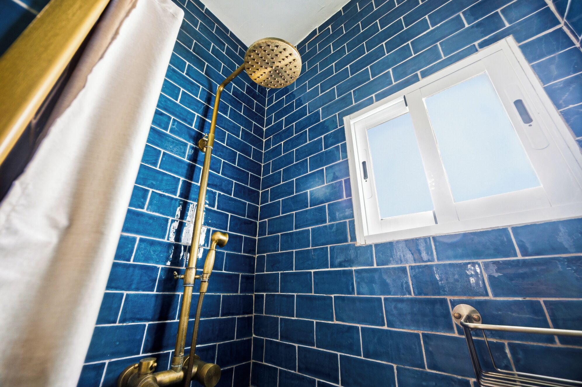 Een badkamer met blauwe betegelde wanden, een douchekop en een raam.
