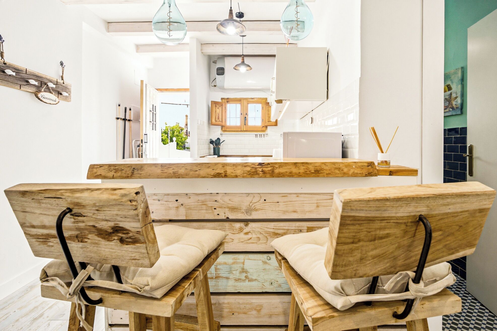 A rustic wooden dining table with two chairs, a kitchen area with wooden cabinets, and pendant lighting.