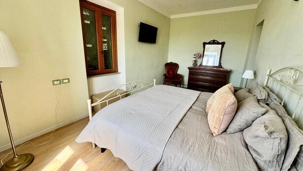 Een slaapkamer met een bed, een dressoir, een stoel, een televisie en een raam met houten kader.