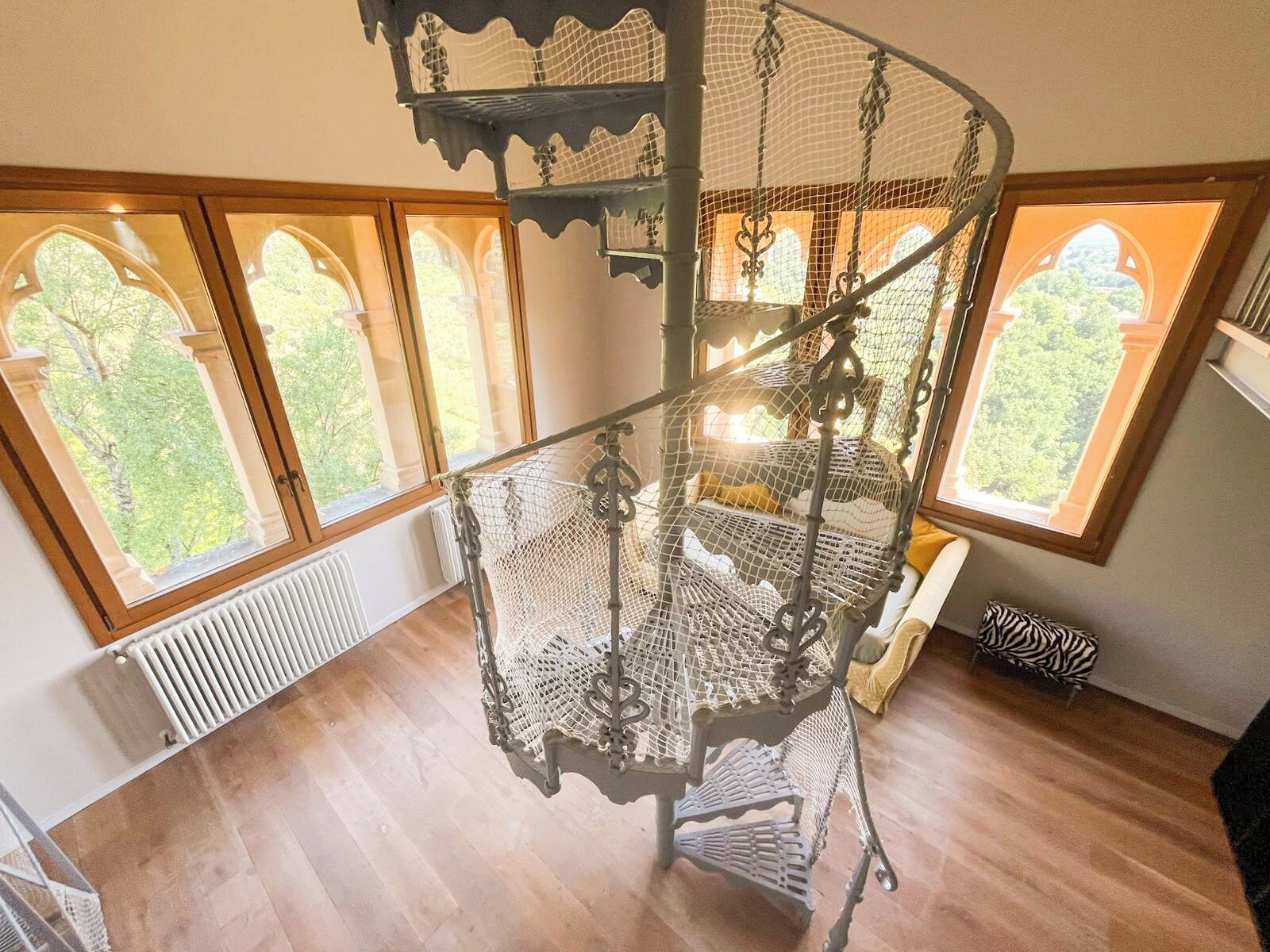 A spiral staircase with a wrought iron design, large windows with arched tops, and a radiator on the floor.