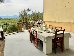 Ein Essbereich im Freien mit einem Tisch für vier Personen, umgeben von Stühlen, auf einer Terrasse mit Blick auf Grünflächen und Berge.